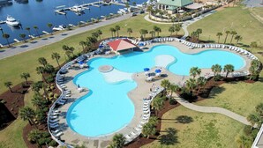 Ein großer, geschwungener Pool mit Liegestühlen und Palmen, umgeben von einer Marina und einem Gebäude mit Gründach.