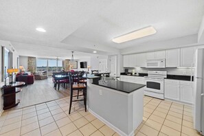 A modern kitchen with white cabinets, a large island, and a dining area with a view.