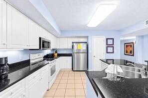 A modern kitchen with white cabinets, stainless steel appliances, and black countertops. - Large Elegant Condo with Waterway View, Onsite Day Spa | Yacht Club Villas - 1-1004 (North Myrtle Beach)