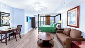 Ein Hotelzimmer mit Bett, Schreibtisch, Sessel, Sofa, Fernseher und Deckenventilator.