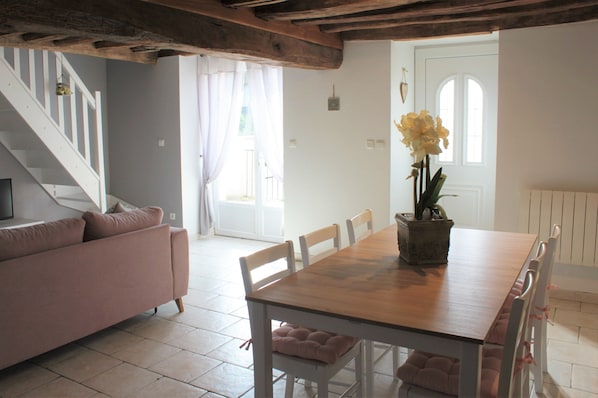 A dining area with a wooden table and white chairs, a pink sofa, and a staircase in the background.