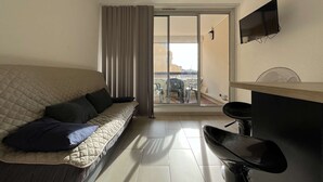 A compact living space with a sofa, a small table, a TV mounted on the wall, and a sliding glass door leading to an outdoor area. - Studio cabin with pool, sleeps 4, Gruissan (Gruissan)