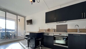 A modern kitchen with black cabinets, a built-in oven, a microwave, and a large window overlooking a terrace. - Studio cabin with pool, sleeps 4, Gruissan (Gruissan)