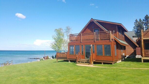 En stuga byggd av trä med en balkong, stora fönster och utsikt över havet.