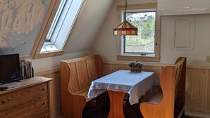 A cozy room with a sloped ceiling, a wooden desk, a table with a blue tablecloth, and a hanging lamp.