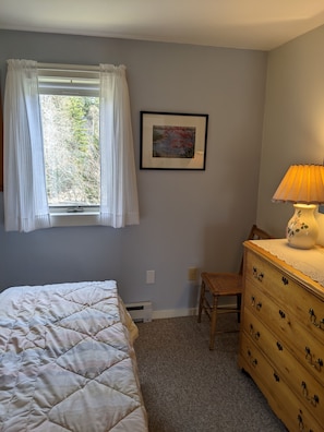 Un dormitorio con cama, cómoda, silla, ventana con cortinas e imagen enmarcadas en la pared.