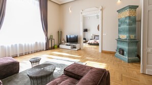 Ein großzügiges Wohnzimmer mit großem Fernseher, bequemen Sitzgelegenheiten, einem Kamin und Blick ins Schlafzimmer.
