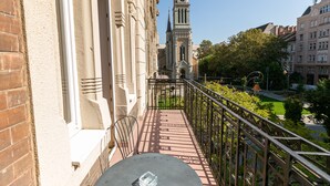 Ein Balkon mit Tisch und Stühlen, der Blick auf eine Stadtlandschaft mit historischen Gebäuden und einem Kirchturm bietet.