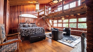 A wooden cabin interior with a bed, seating area, and large windows.