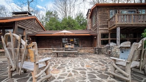 A rustic cabin with a stone patio, outdoor seating, and a covered dining area.