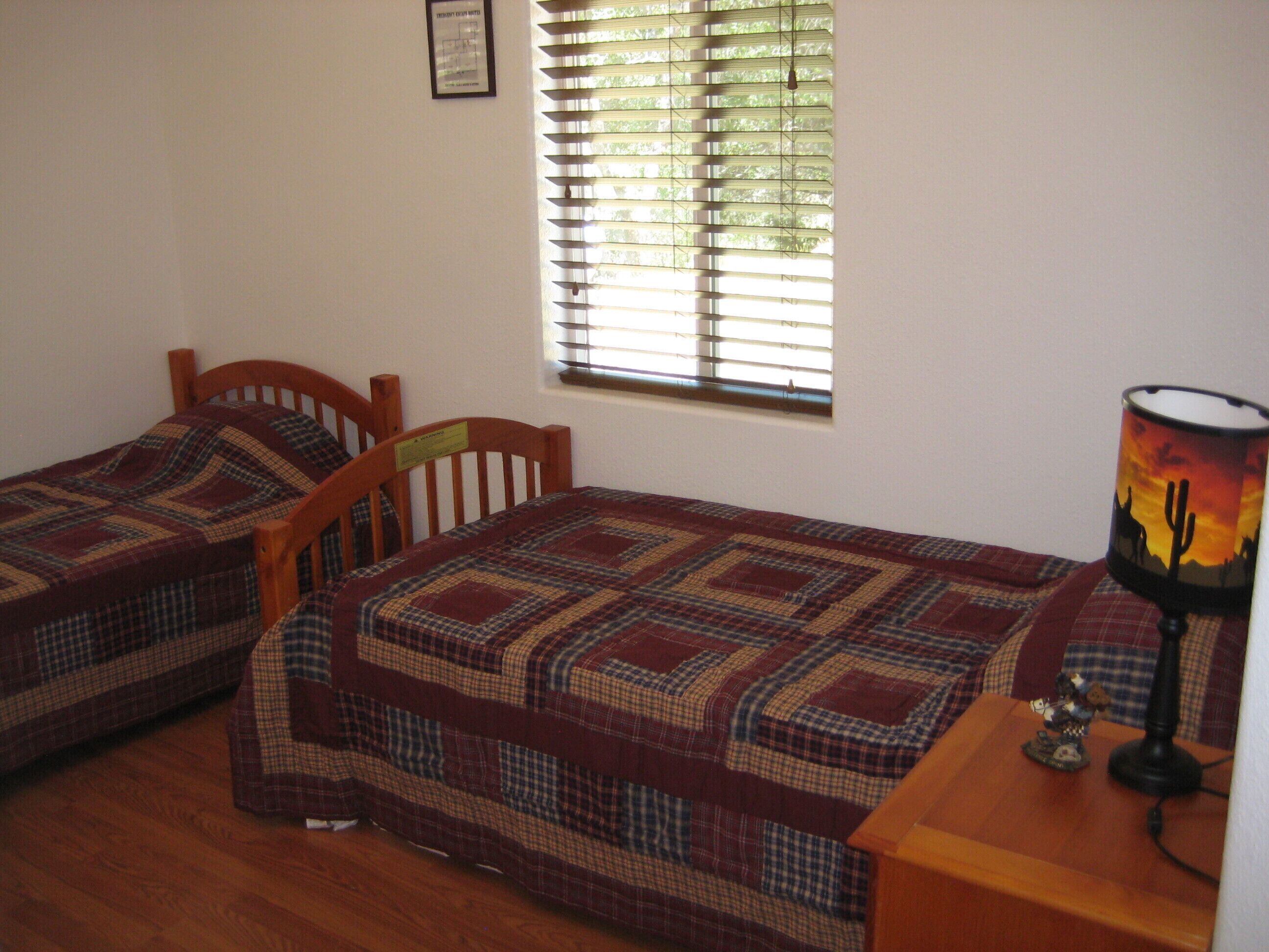 A bedroom with two single beds, a window with blinds, a lamp, and a framed picture on the wall.