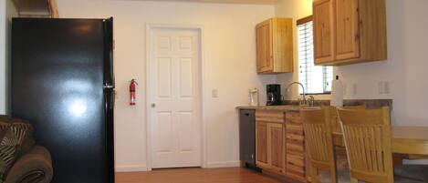 Una cocina compacta con armarios de madera, un refrigerador negro, una cafetera y un comedor con sillas de madera.