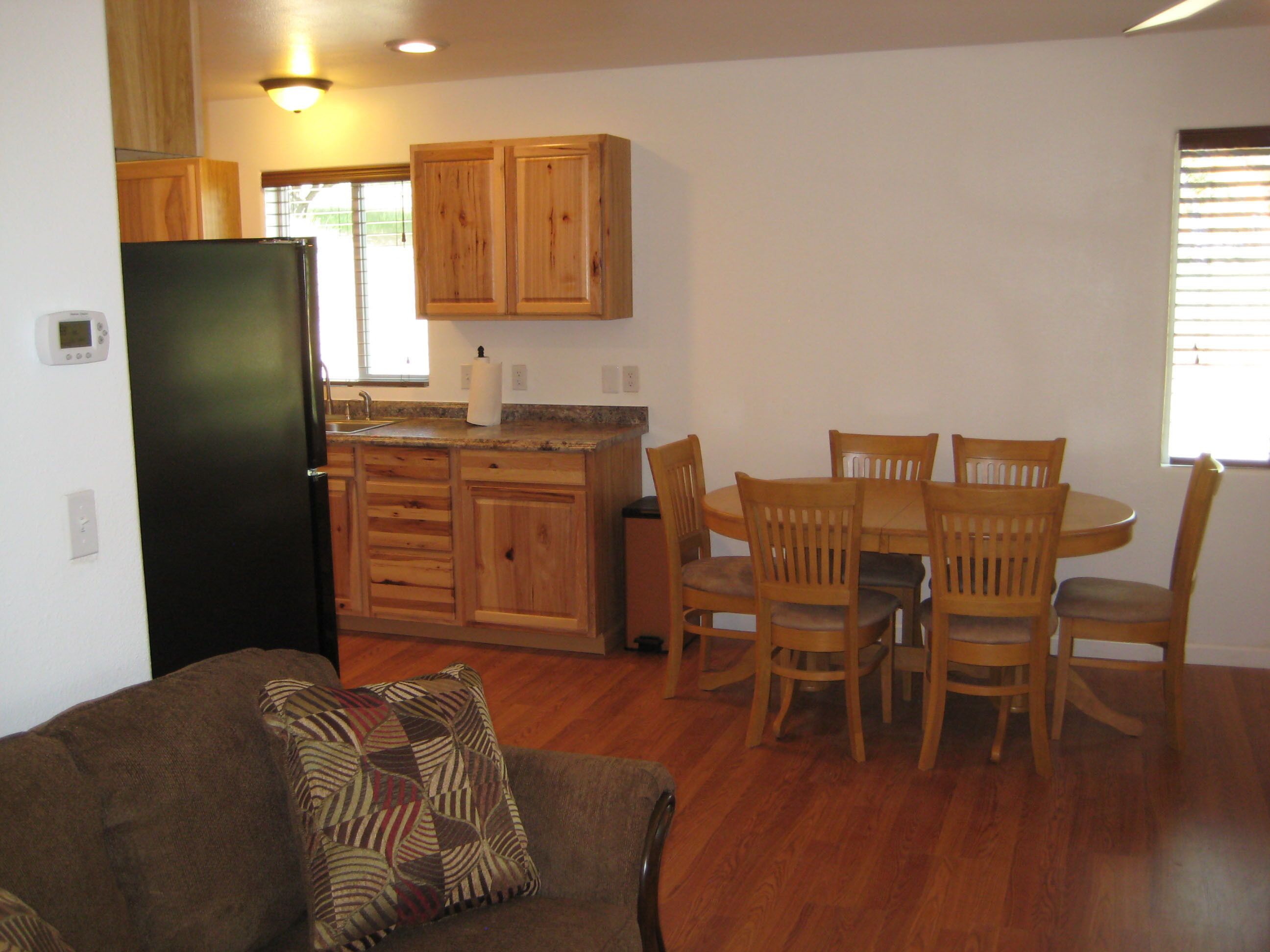A compact kitchen with wooden cabinets, a black refrigerator, and a dining area with a round table and chairs.