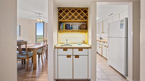 A compact kitchen with white cabinets, a built-in wine rack, and a dining area with a wooden table and chairs. - Oceanfront condo in private community + Free Attraction Tickets! (Myrtle Beach)