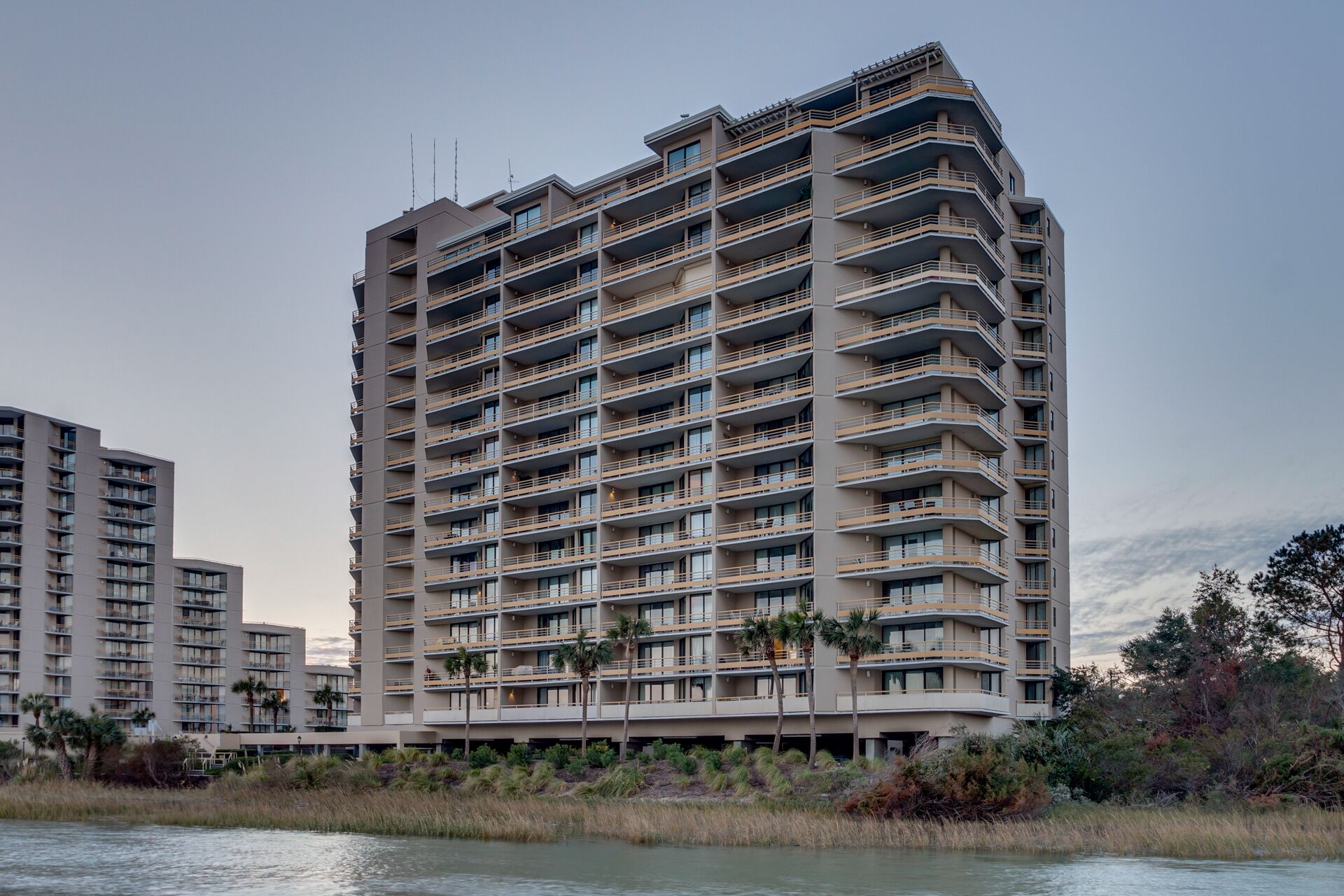 A multi-story hotel with balconies, located near a body of water.