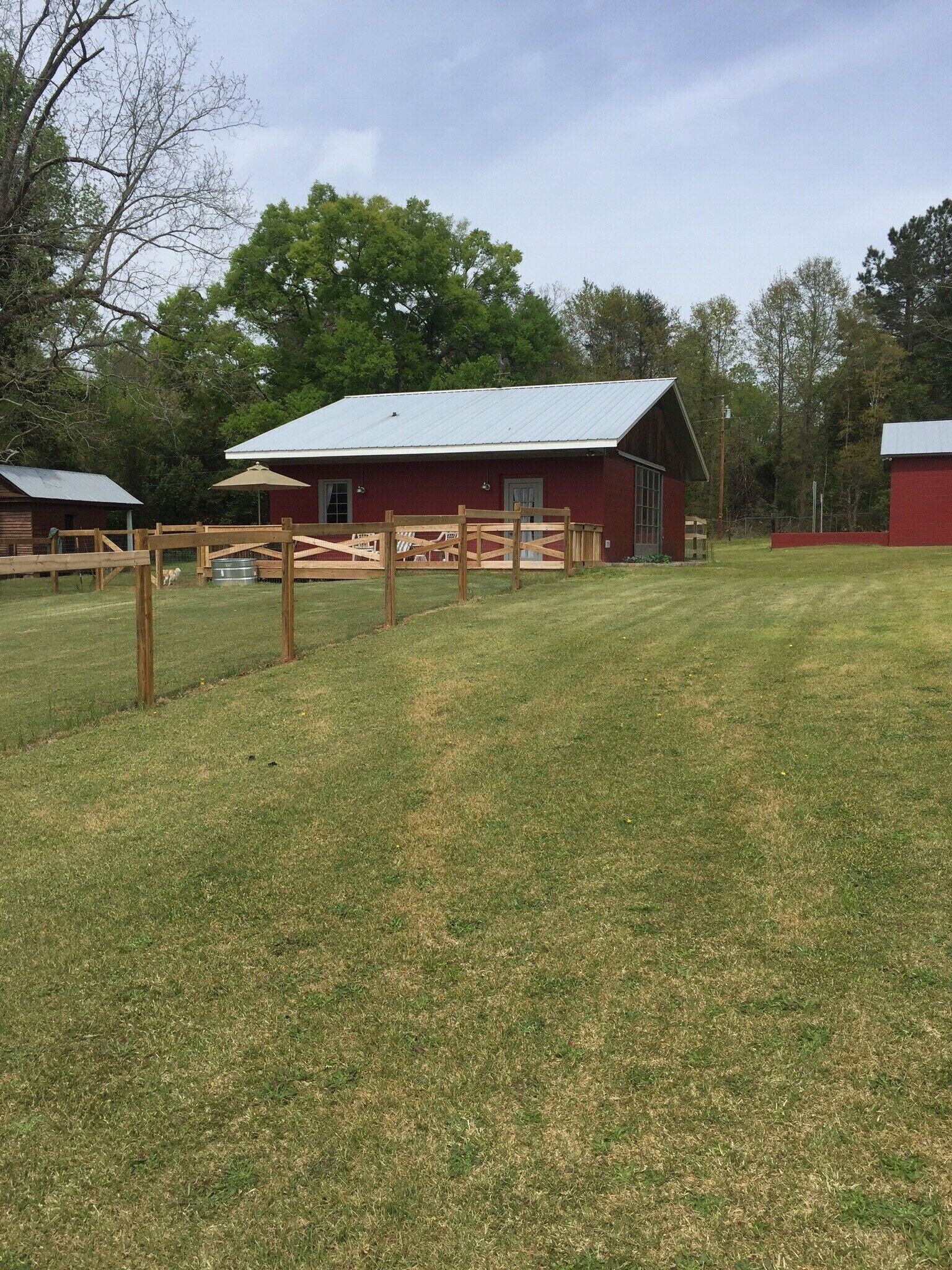 A red barn with a metal roof, surrounded by a wooden fence and a grassy field.
