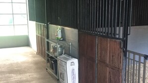 A stable interior with a metal rack holding supplies, a white container, and a metal gate.