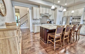 A kitchen with wooden cabinets, a central island with chairs, and a staircase leading to another level.