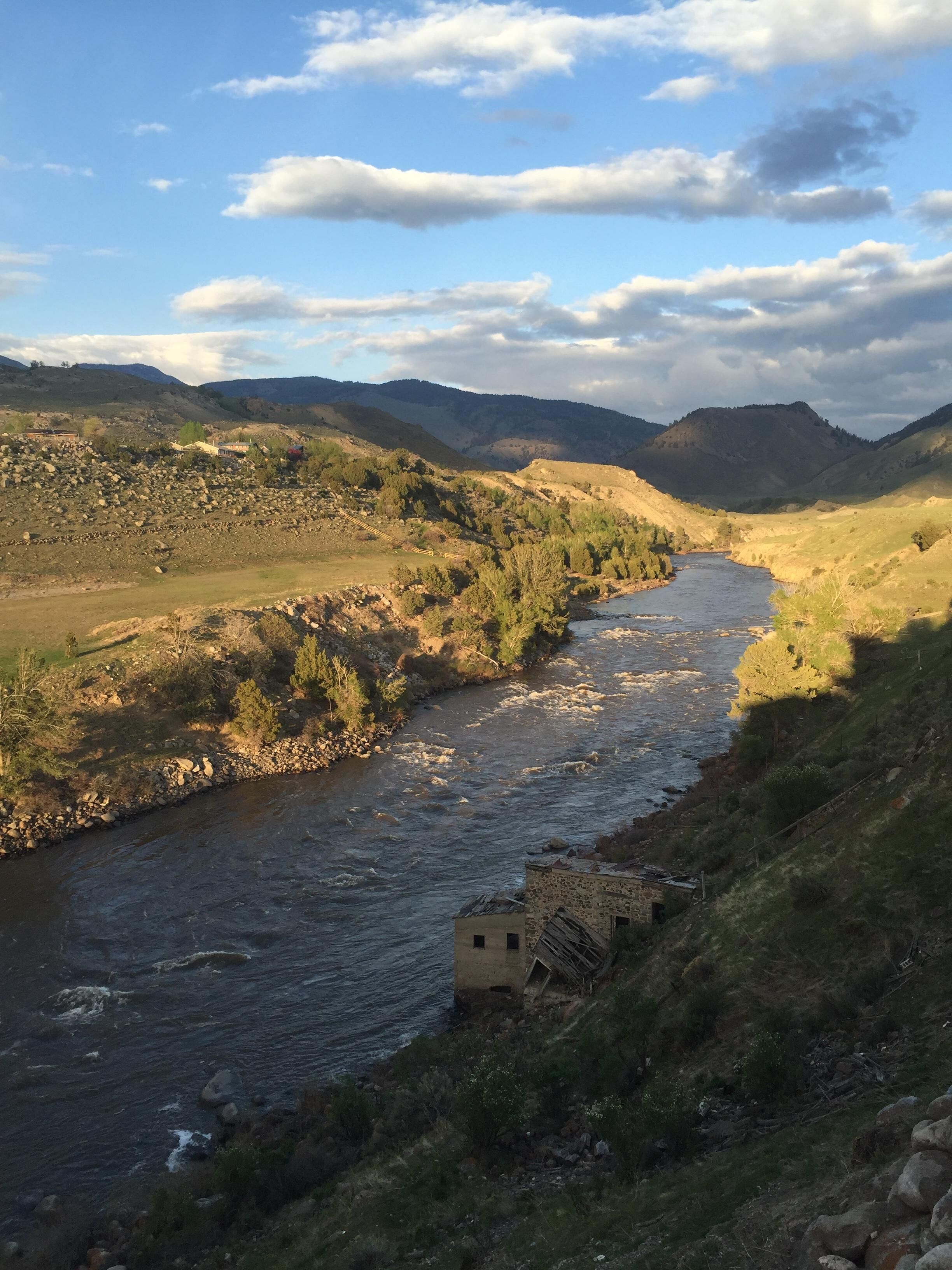 A river flowing through a valley with a small building near the water's edge.