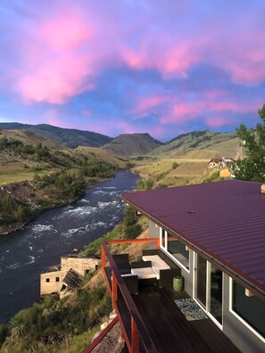 Una casa moderna con terraza que da a un río y colinas.