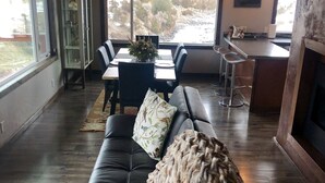 A spacious living area with a black leather sofa, a dining table with chairs, and a kitchen area with a bar.