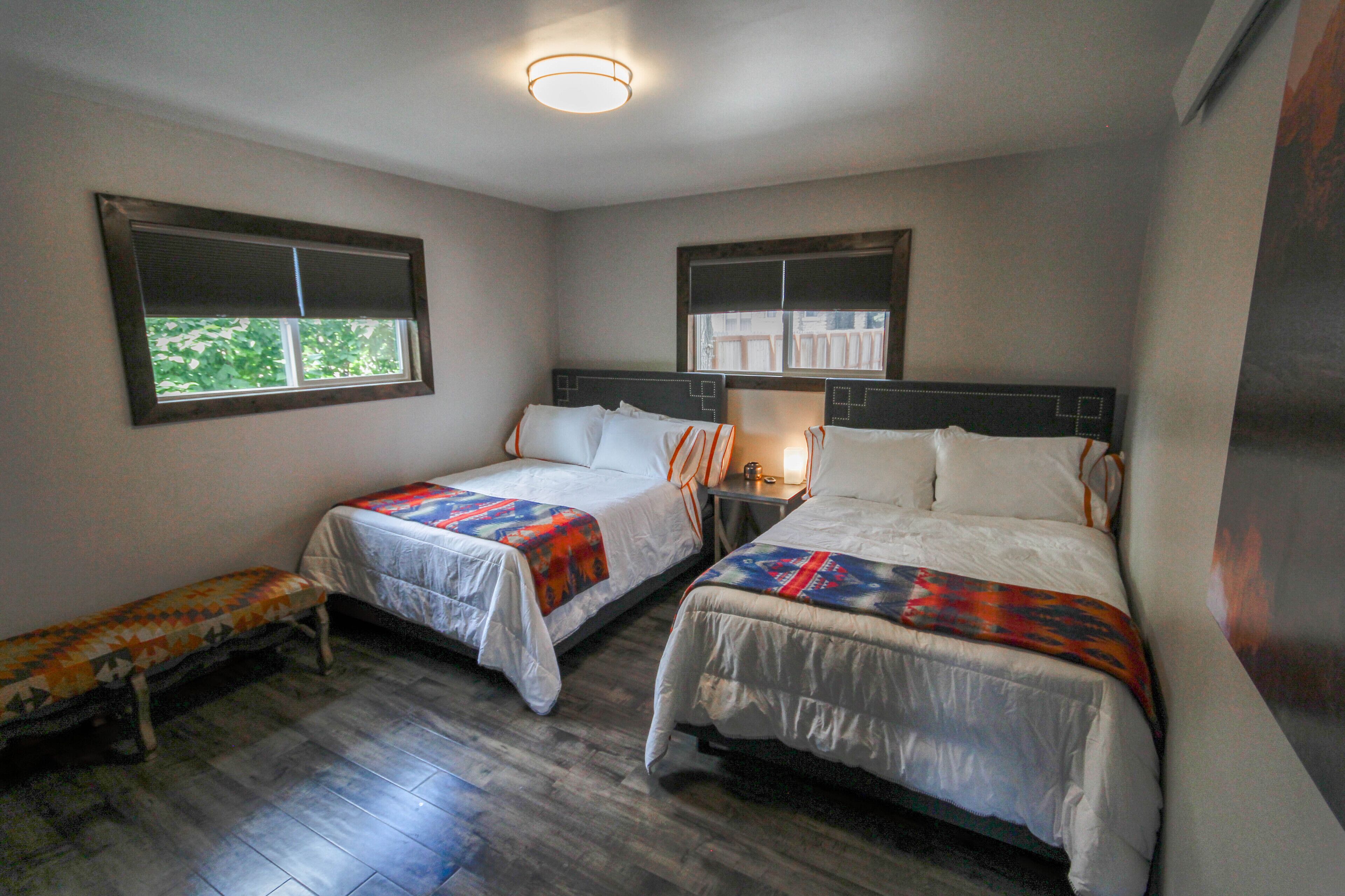 A hotel room with two single beds, a bench, and a window.