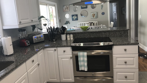 A modern kitchen with white cabinets, a granite countertop, a built-in oven, and a stainless steel range hood. - Fully Fenced in Backyard, 1 block to the beach, Golf Cart included, (Myrtle Beach)