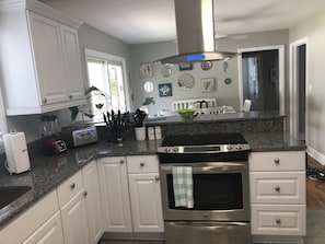 A modern kitchen with white cabinets, a granite countertop, a built-in oven, and a stainless steel range hood.