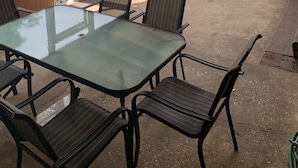 A covered patio area with a glass table and metal chairs, wooden ceiling beams, and a view of a residential neighborhood. - Fully Fenced in Backyard, 1 block to the beach, Golf Cart included, (Myrtle Beach)