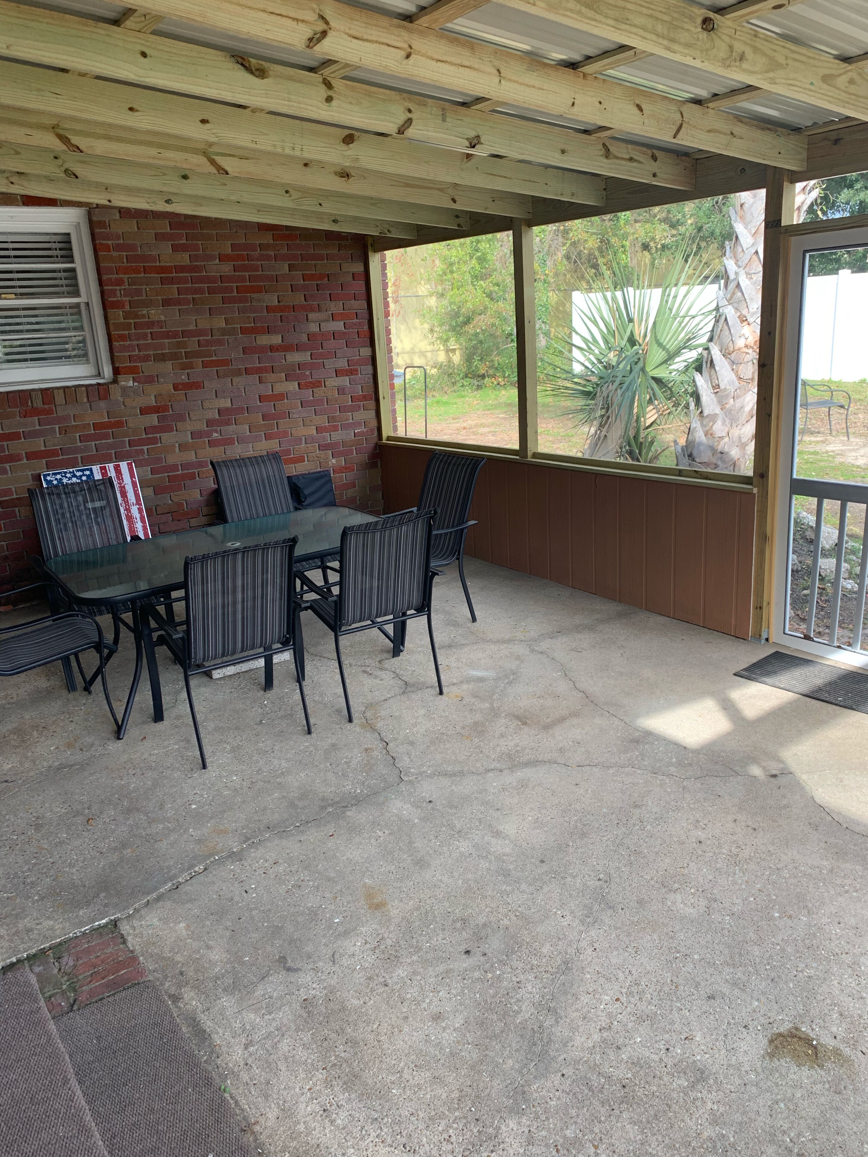 Une terrasse couverte avec un mur en briques, une table en verre et des chaises.