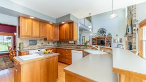 Une cuisine spacieuse avec des meubles en bois, un grand îlot central et un mur d’accent en pierre.
