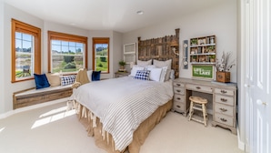 Une chambre à coucher avec un grand lit, une tête de lit en bois, un coin fenêtre aménagé en siège, une commode et une bibliothèque.
