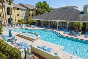 Une piscine dotée de chaises longues et d’un jacuzzi, le tout entouré d’un bâtiment comportant de nombreux balcons.