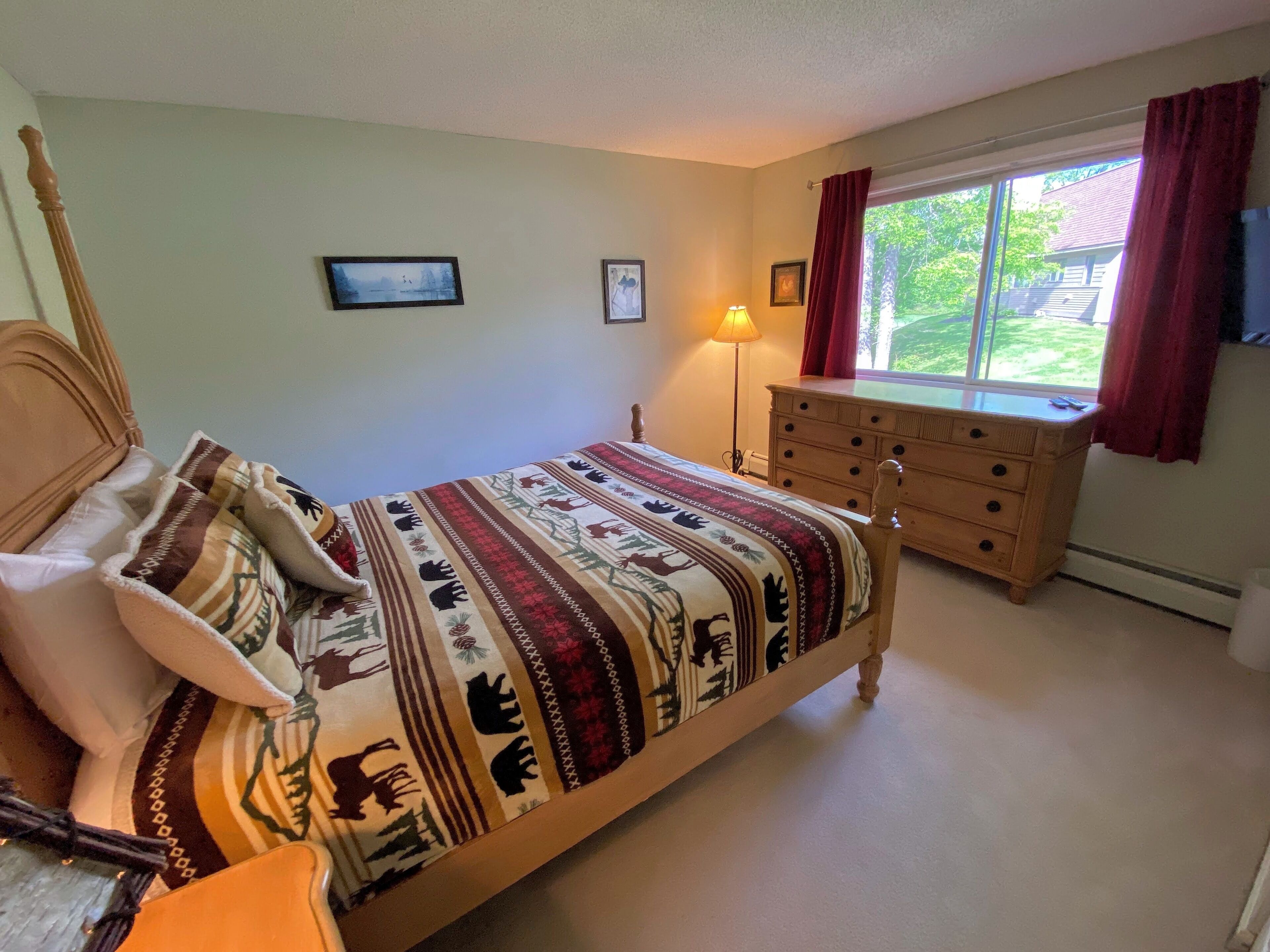 Een slaapkamer met een bed, een dressoir, een lamp en een raam met gordijnen.