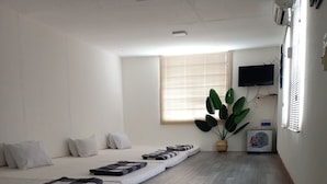 A hotel room with a long bed, a small table with a plant, a TV mounted on the wall, and a window with blinds. - Tan An Guest House (Ho Chi Minh City)