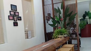 A long wooden bench with matching stools, a wall with framed pictures, and a decorative partition with plants. - Tan An Guest House (Ho Chi Minh City)