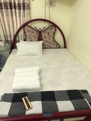 A neatly made bed with a floral headboard, a white pillow, and folded white towels. - Tan An Guest House (Ho Chi Minh City)