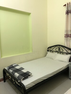 A small, single-bed room with a simple metal frame, a plain mattress, and a checkered blanket. - Tan An Guest House (Ho Chi Minh City)