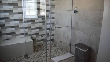 Ein Badezimmer mit Duschkabine aus Glas, Fliesenboden, Waschbecken und Mülleimer.