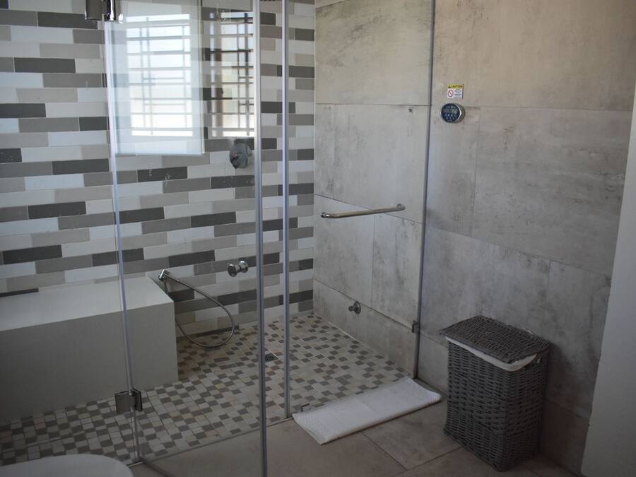Ein Badezimmer mit Duschkabine aus Glas, Fliesenboden, Waschbecken und Mülleimer.