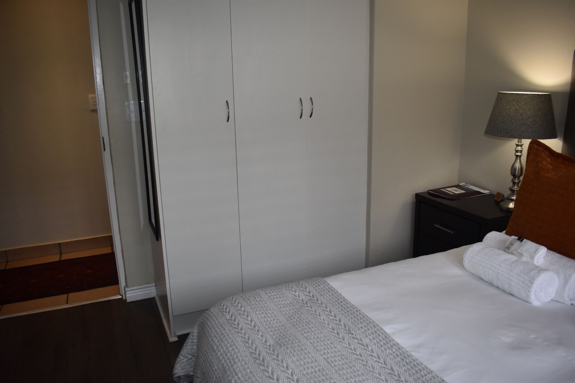 A bedroom with a bed, a nightstand, a lamp, and a wardrobe.