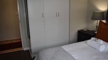 A bedroom with a bed, a nightstand, a lamp, and a wardrobe.