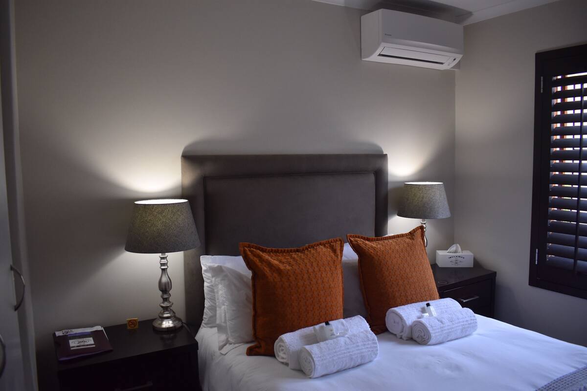 A neatly made bed with white linens, two orange pillows, and two bedside lamps.