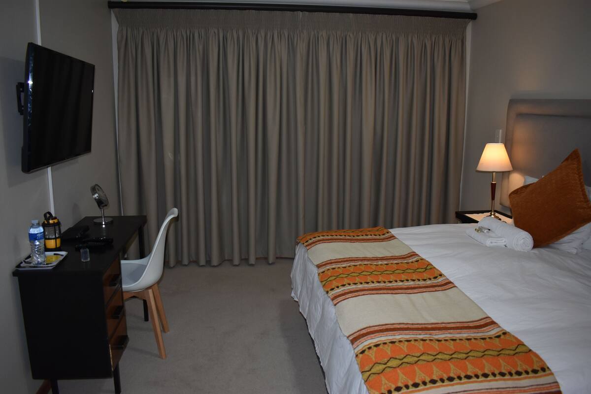 A hotel room with a bed, a desk, a chair, a television, and a window with curtains.