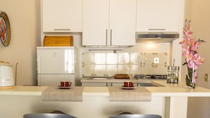 A modern kitchen with white cabinets, a stainless steel range hood, and a tiled backsplash. There are two bar stools with a checkered table runner. - Blue Wood Apartment (Letojanni)