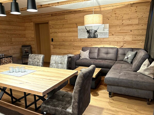 Una sala de estar moderna con una pared de madera, un sofá seccional, una mesa de comedor y una lámpara colgante.