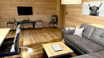 A modern living room with a fireplace, a grey sofa, a wooden coffee table, and a mounted television.