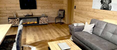 Una sala de estar moderna con chimenea, un sofá gris, una mesa de centro de madera y un televisor montado.