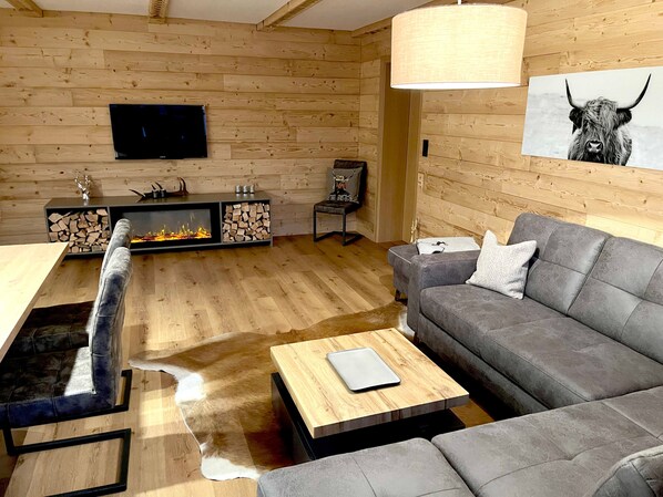Una sala de estar moderna con chimenea, un sofá gris, una mesa de centro de madera y un televisor montado.