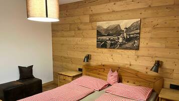 A wooden-paneled room with a bed, two bedside tables, a lamp, a chair, and a wall-mounted picture.